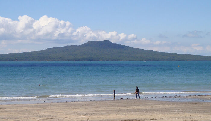 Beach with two people near the water and a forested island in the distance, representing forgotten tourist destinations.
