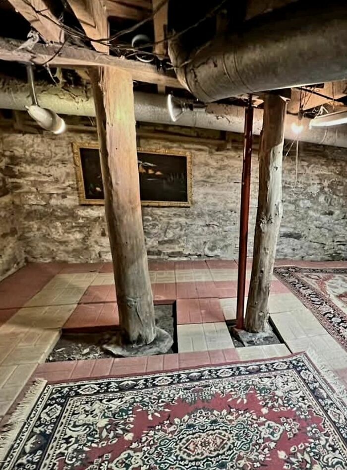 Basement with exposed wooden support beams, stone walls, and patterned rugs in a home with a hidden, forgotten past.