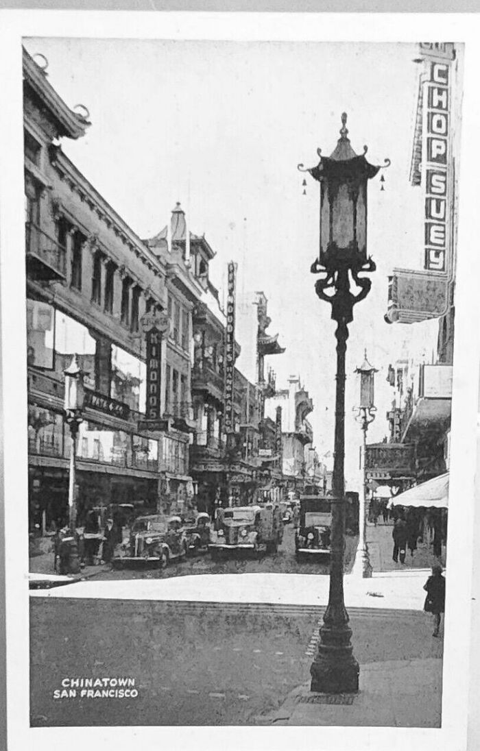 Vintage black and white photo of San Francisco Chinatown street scene with old cars and traditional architecture.