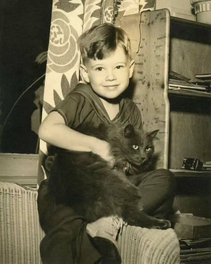 Vintage photo of a young boy holding a fluffy cat, showcasing the timeless bond between kids and cats in a cozy home setting.