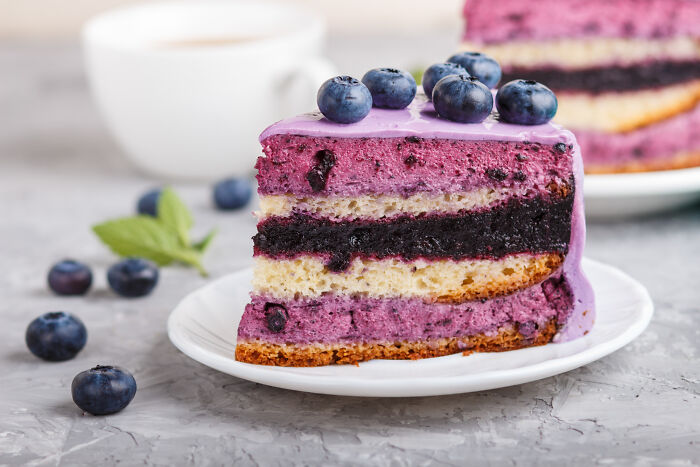 Slice of blueberry layer cake with purple frosting and fresh blueberries, representing wild cooking opinions and internet food trends.