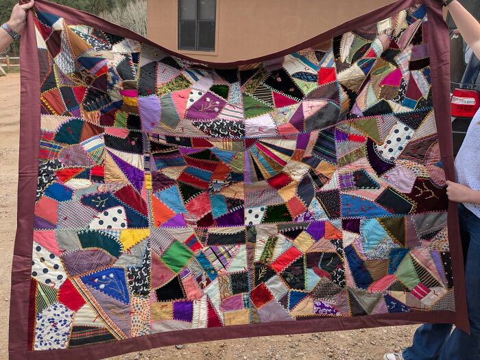 Colorful thrifted patchwork quilt held open outdoors showcasing unusual and wonderful vintage fabric patterns.