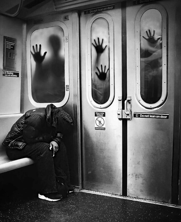 Black and white street photo of person sitting on subway bench with ghostly hands pressed on train doors.