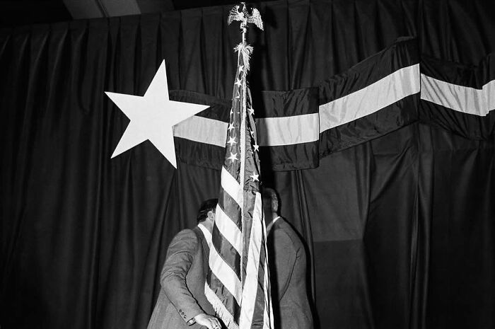 Black and white street photo featuring two men with an American flag and large star symbol in background.