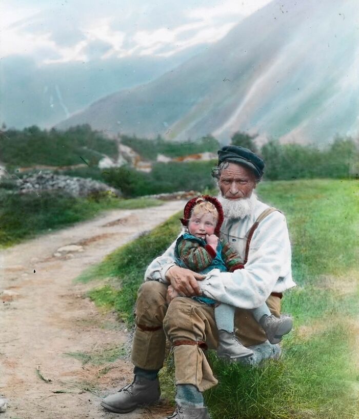 Elderly man holding a child outdoors, showcasing vibrant cultural past in a colorized historical photo.