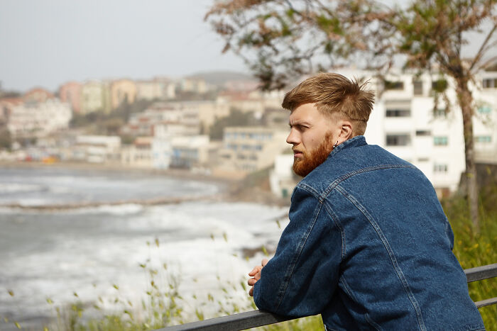 Young man in denim jacket gazing over the ocean, reflecting on moments that feel like being picked last in gym class.