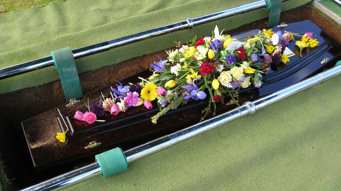 Coffin in a grave surrounded by green grass with a colorful arrangement of flowers on top, reflecting harsh life advice.