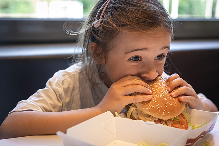 Young girl eating a large burger, illustrating the topic of feeding nieces junk food for multiple days.