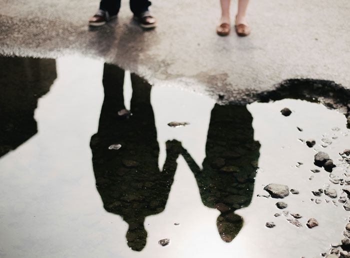 Reflection of a teen son and girlfriend holding hands near a puddle, symbolizing teen son get girlfriend pregnant on purpose.