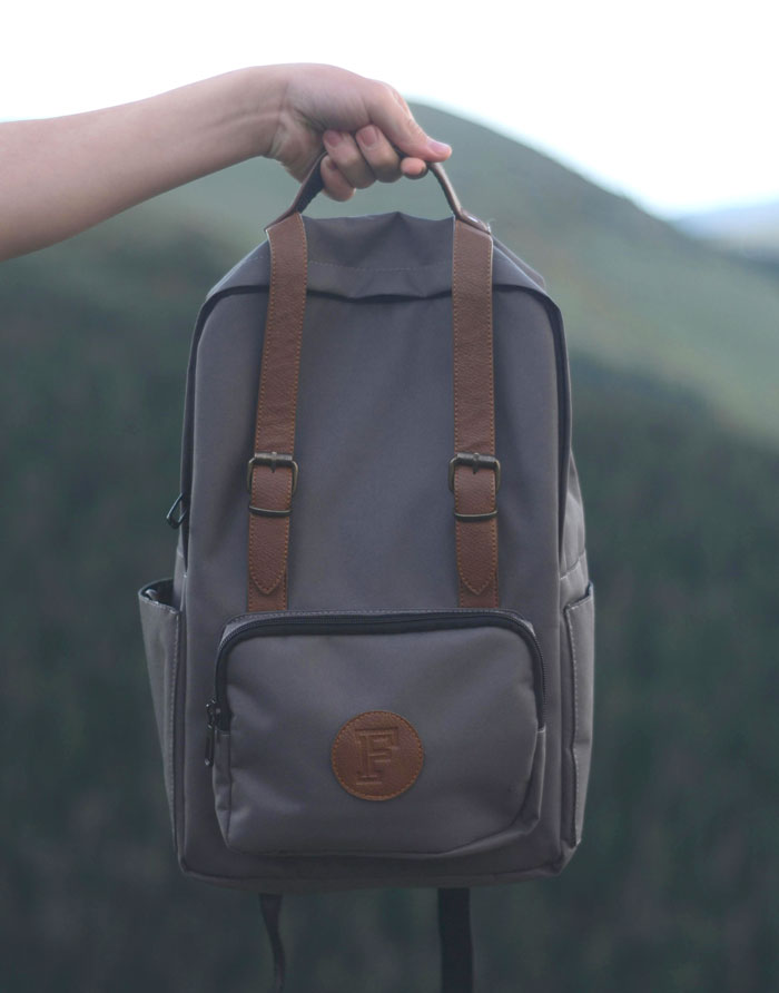Hand holding gray backpack with brown straps, symbolizing stories of unsuccessful mugging attempts by strangers.