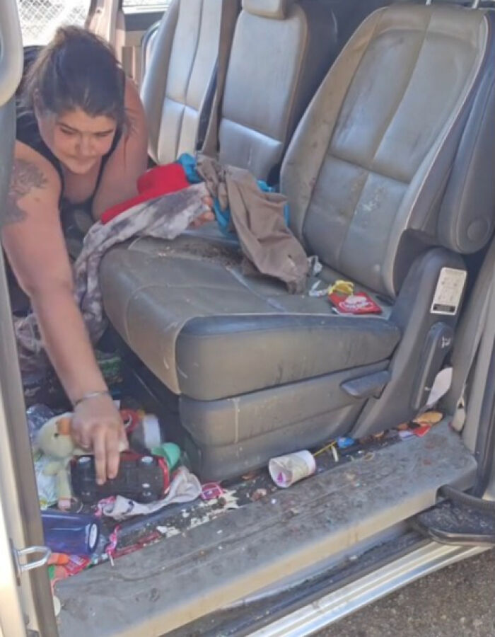 Woman cleaning out filthy car interior cluttered with trash and dirty clothes, addressing tired internet reactions.