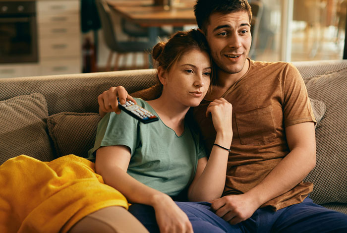 Couple sitting on couch watching TV together, capturing a moment of curiosity about secrets in marriage.
