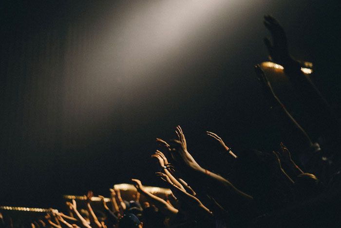 People raising hands in a dark room under spotlight, symbolizing stories of people who escaped from cults sharing experiences.