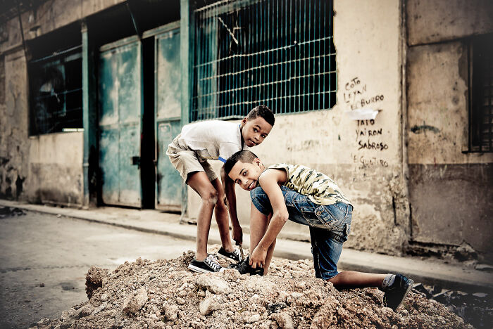 Two boys on a dirt pile in an urban setting, captured in a lively street photography moment by talented photographers.