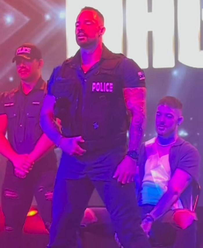 Man dressed as police officer performing on stage with others, related to former pole dancer turned monk attention seeker story.