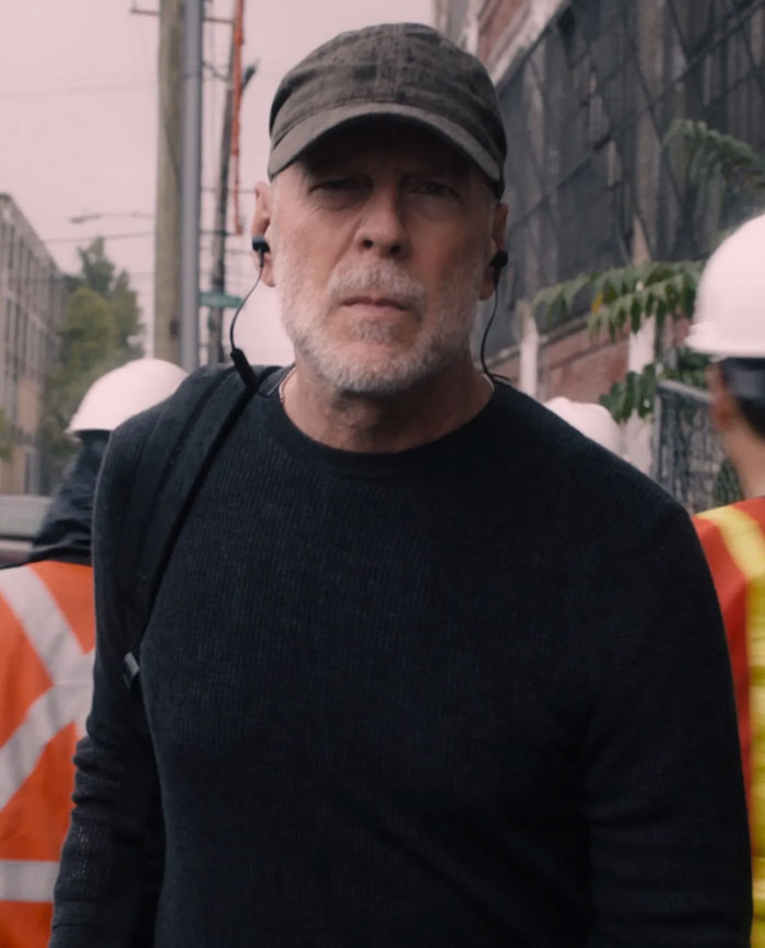 Man wearing a cap and earbuds walking outdoors with construction workers, depicting a celebrity encounter moment.