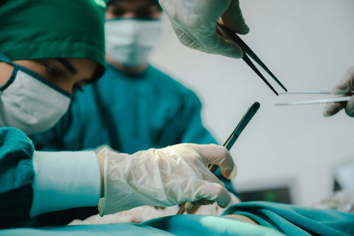 Equipo de expertos en autopsias realizando un examen detallado con herramientas médicas en un quirófano moderno.