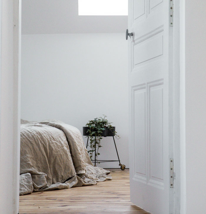 Minimalist bedroom with neutral bedding and a plant stand, illustrating weird parent rules you thought were normal.