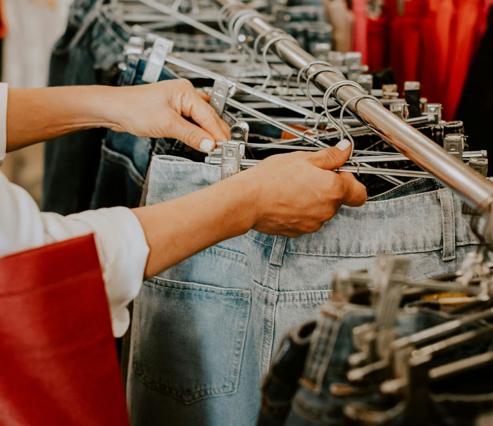 Person browsing denim jeans on a rack, illustrating common ways people lose money while saving on purchases.