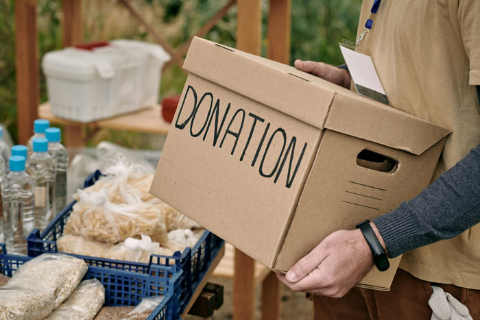 Person holding a donation box near food supplies, illustrating habits linked to being raised poor.