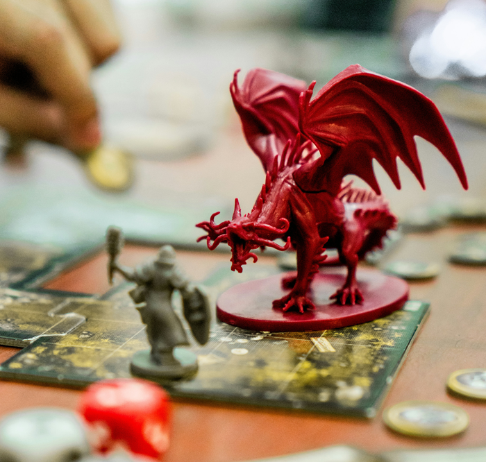 Close-up of a red dragon game piece and a warrior figurine on a board, illustrating intense fantasy gameplay and strategy.