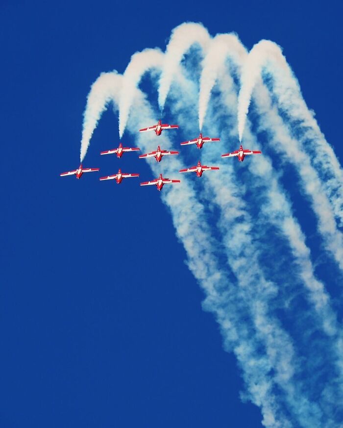 Red planes forming a creative photo edit with smoke trails against a clear blue sky in good visual lies style.