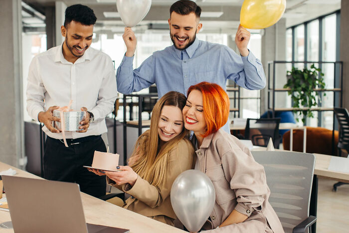 Four coworkers celebrating with balloons and gifts during office party, capturing moments from adult life feeling left out.