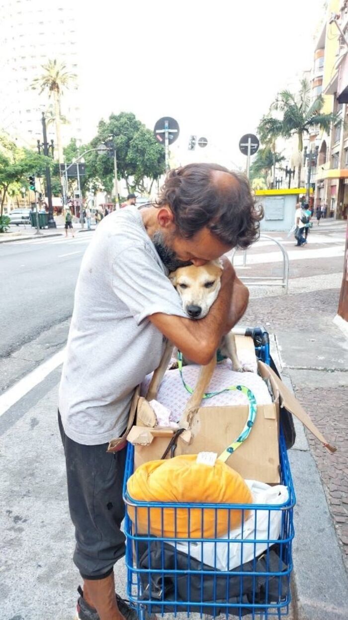 Homeless man hugging his dog on a city sidewalk, showing strong bond in photos documenting lives of homeless people and dogs.