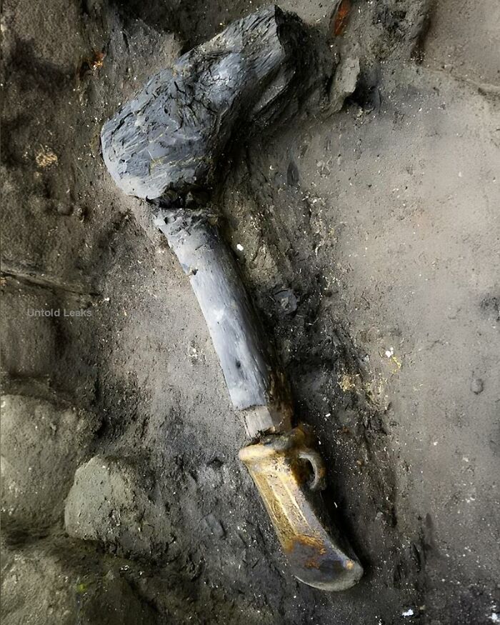 Ancient history artifact resembling a large stone tool or weapon partially buried in dirt and soil.