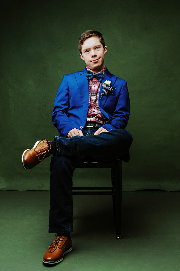 Teen with Down syndrome wearing blue blazer and bow tie, sitting confidently against green background celebrating inclusion.