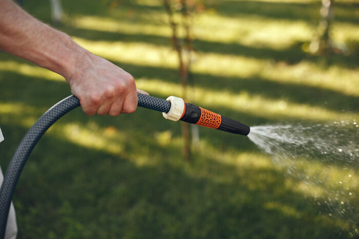 Hand holding garden hose spraying water outdoors, illustrating casual things that can be deadly risks.