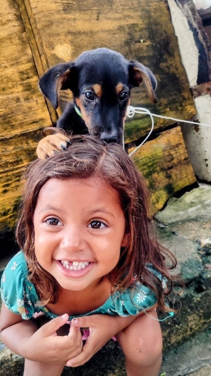 Smiling child playing with a small dog on her head, highlighting the lives of homeless people and their dogs.