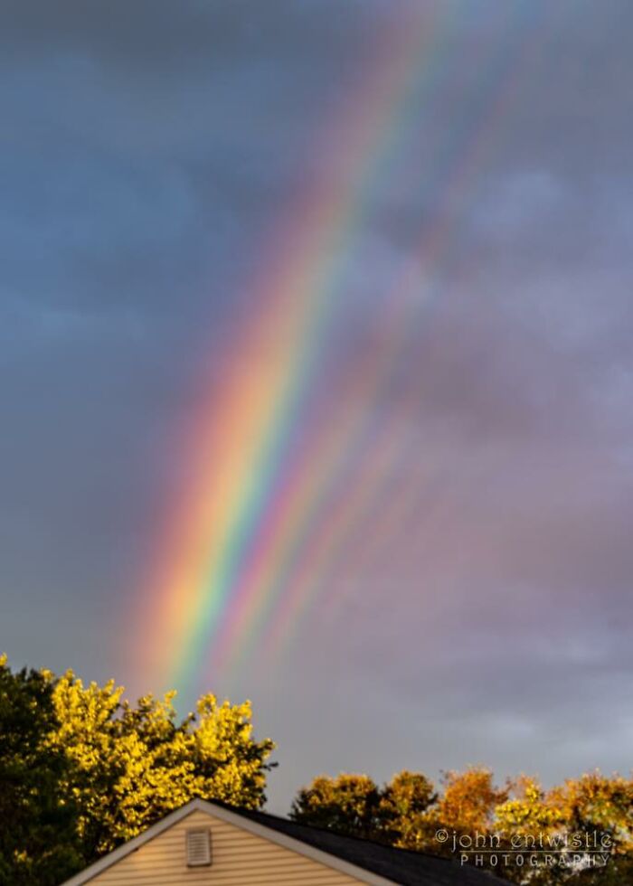 Double rainbow over a house and trees, showcasing one-in-a-million coincidences in a vibrant natural sky.