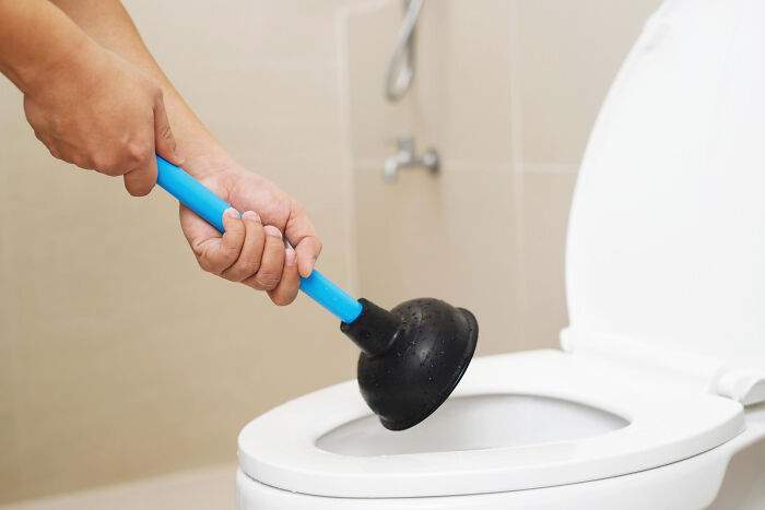 Hand using a plunger on a toilet, representing one of the wildest life blunders people keep secret.