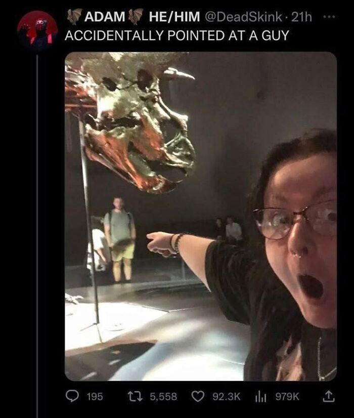 Person with glasses pointing and looking surprised at a dinosaur skull in a museum, funny memes to lighten a hard day.