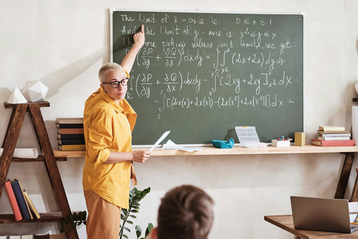 Teacher in a yellow shirt writing complex math equations on a chalkboard, surprising students in the classroom setting.