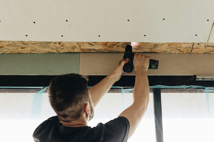 Man using a drill to install drywall, illustrating common ways people lose money while thinking they’re saving.