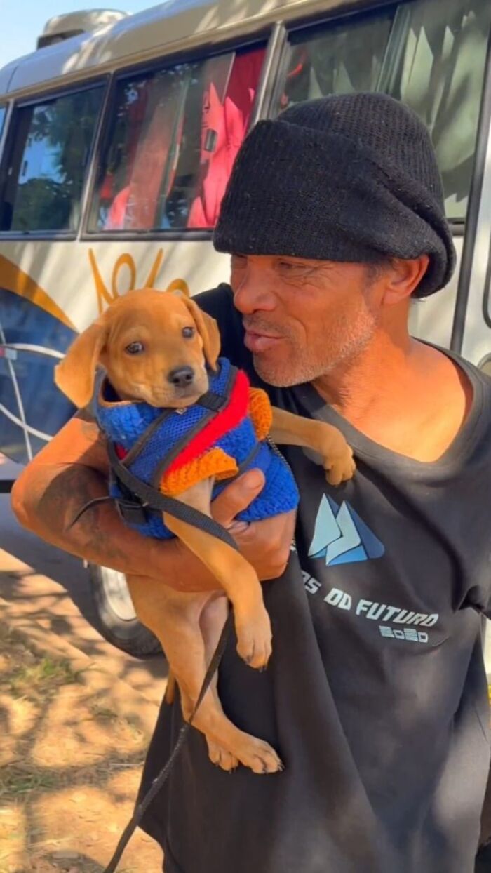 Man wearing black beanie holding small dog in colorful sweater, highlighting lives of homeless people and their dogs.