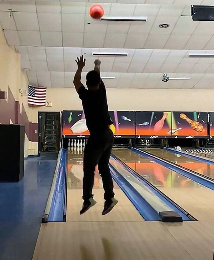 Hombre lanzando bola roja en boliche, imagen maldita por salto inusual y ángulo del tiro inesperado.