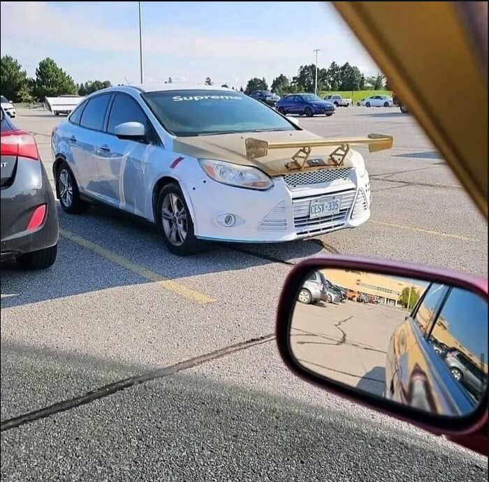 Coche con un alerón casero de madera en el capó, imagen maldita y curiosa en un estacionamiento.