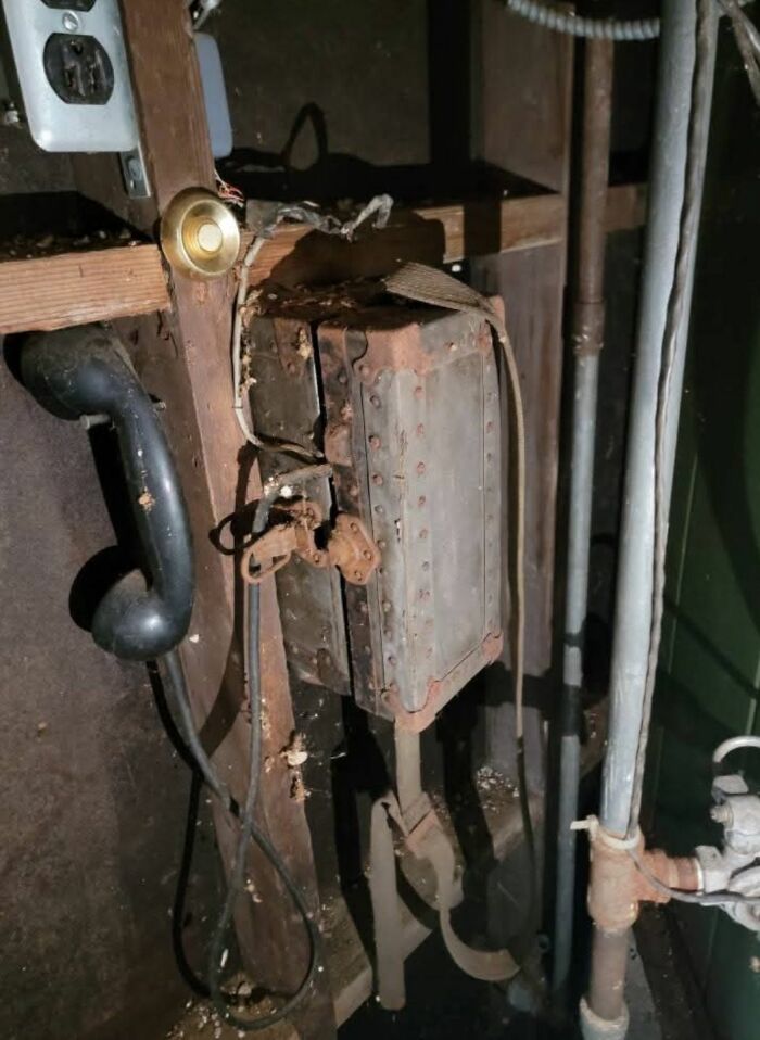 Rusty old telephone and electrical box attached to wooden wall with pipes nearby in a home with hidden past.