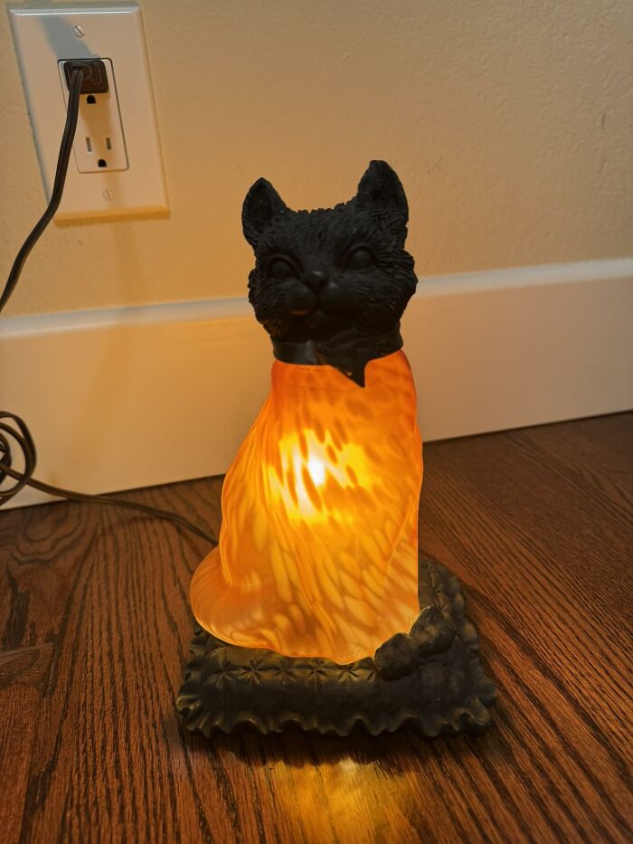 Black cat lamp with glowing orange glass body sitting on wooden floor, a weird and wonderful thrifted find.