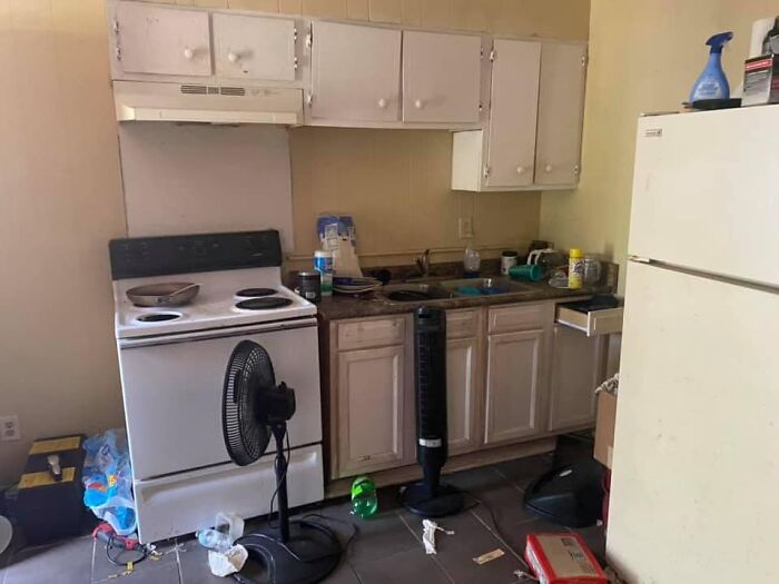 Cluttered and dirty kitchen with old appliances and fans, an example of worst real estate photos for unattractive homes.