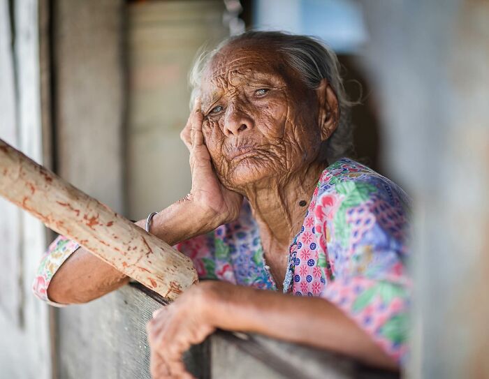 Elderly woman with expressive wrinkles resting her head on her hand in a striking portrait by Massimo Bietti.