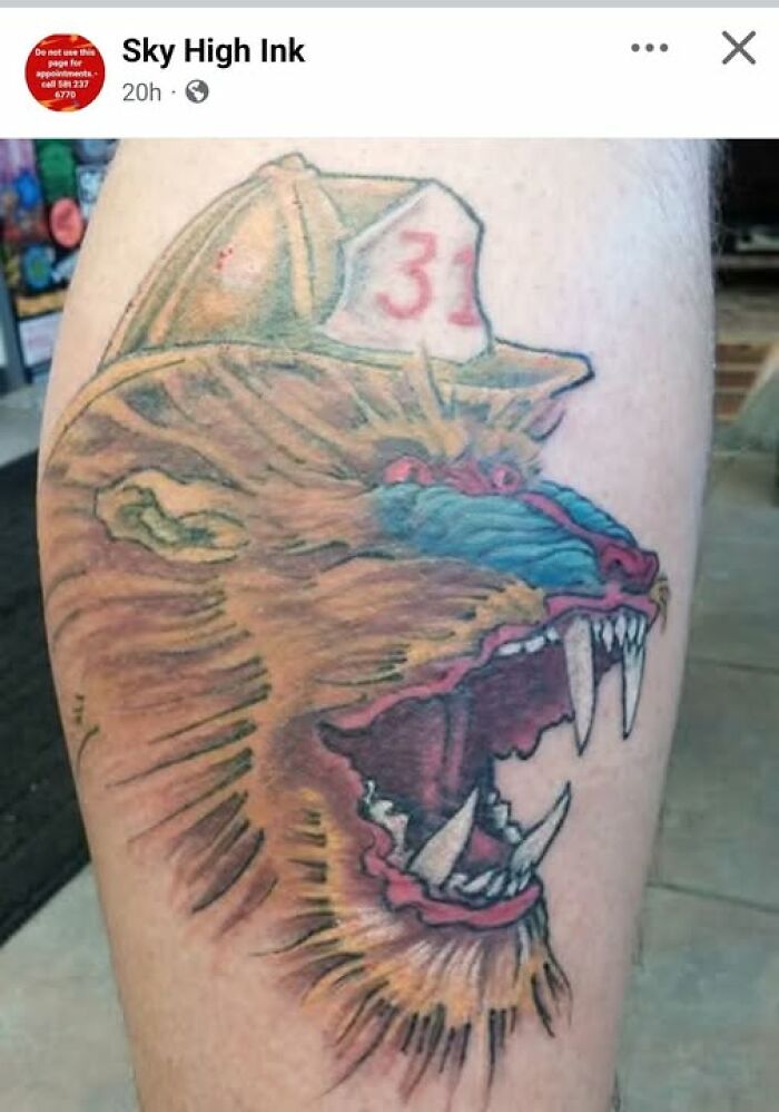 Lion head tattoo with exaggerated teeth and a firefighter hat numbered 31, an example of a permanent tattoo mistake.