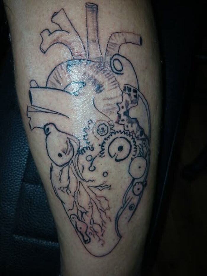 Tattoo of an anatomical heart with mechanical gears inked on a person's leg, a cool design with a permanent mistake.