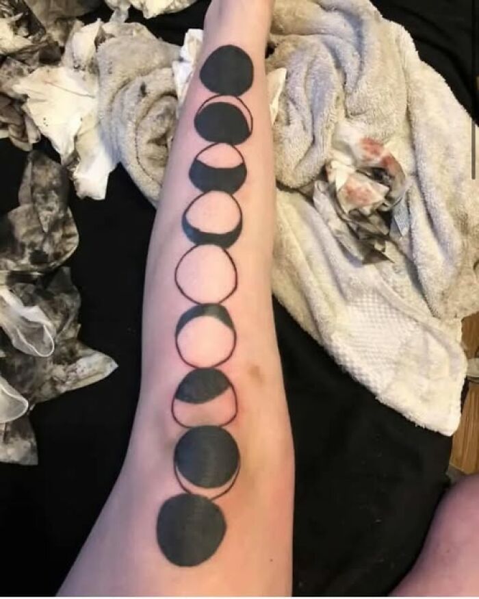 Arm tattoo featuring black circles and crescent shapes but with uneven and inconsistent shading, a permanent mistake in inked design.