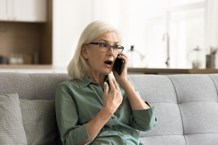 Older woman in glasses reacting with shock while talking on phone, illustrating soul-crushing things parents said.