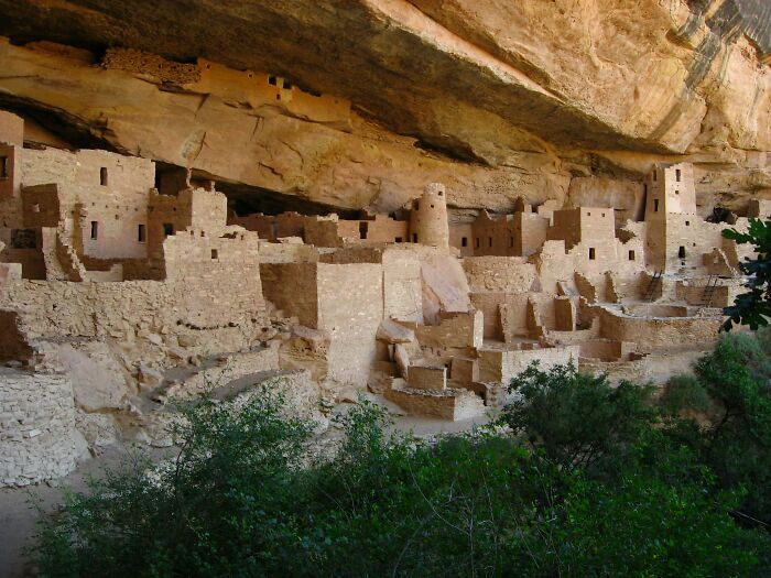 Ancient cliff dwellings showcasing hidden UNESCO gems nestled under a large rocky overhang surrounded by greenery.