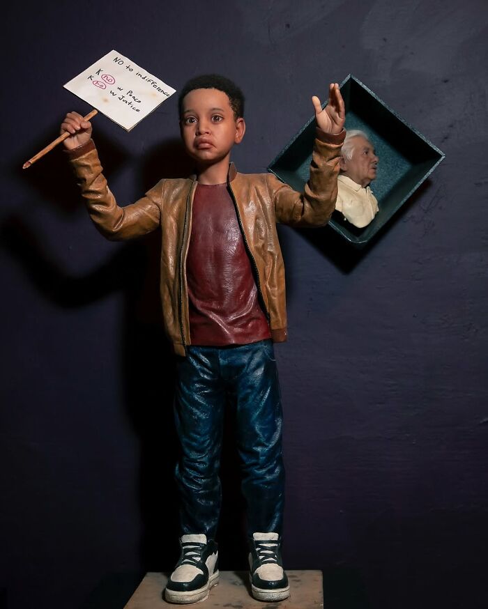 Child sculpture holding a protest sign, showcasing Ruben Orozco Loza's breathtaking realism in lifelike art.